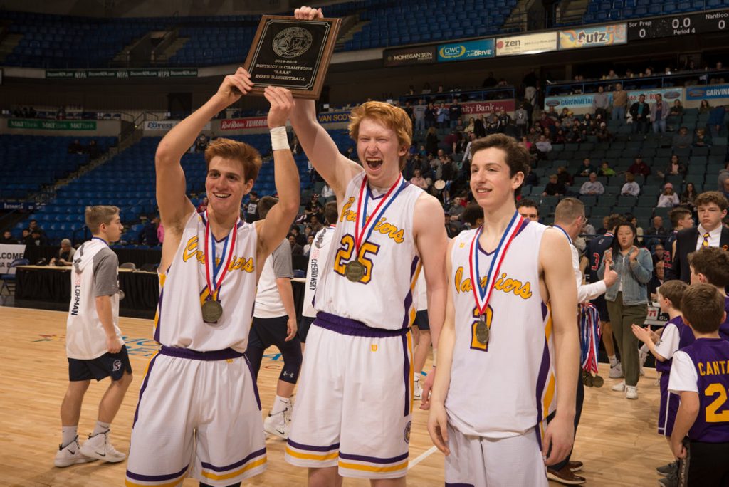 Basketball players hoisting a championship plaque.