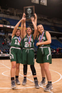 Girls basketball players hoisting championship plaque.