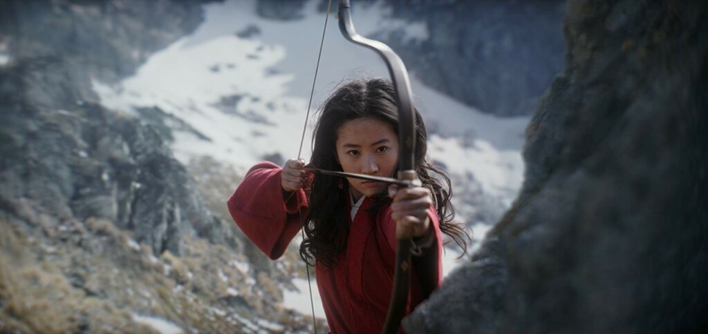 Woman shooting a bow and arrow on a mountain.