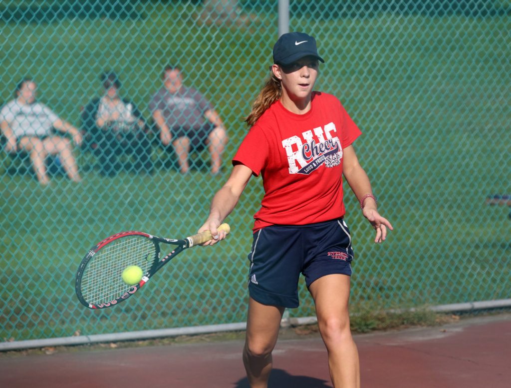 Girl hitting tennis ball to opponent.