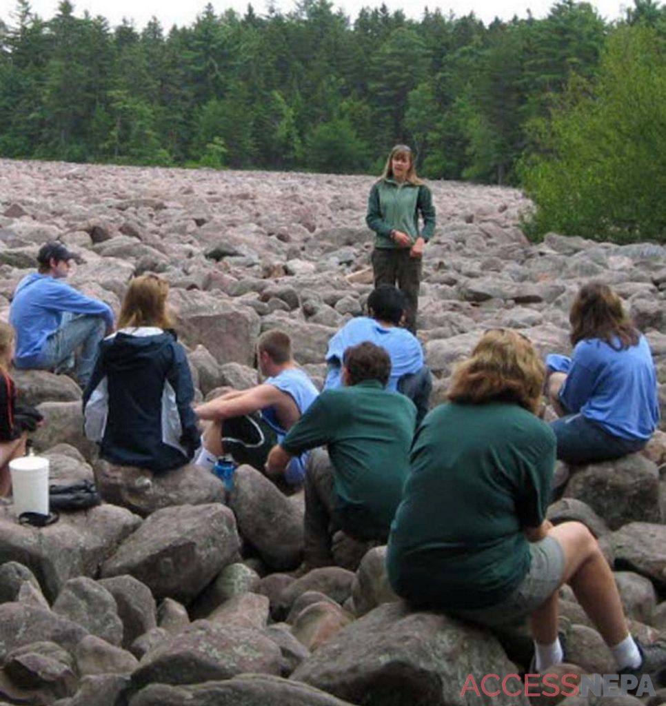 Woman stands facing group sitting on boulders at Boulder Field.