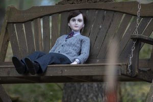 A creepy doll sits on a seat swing.
